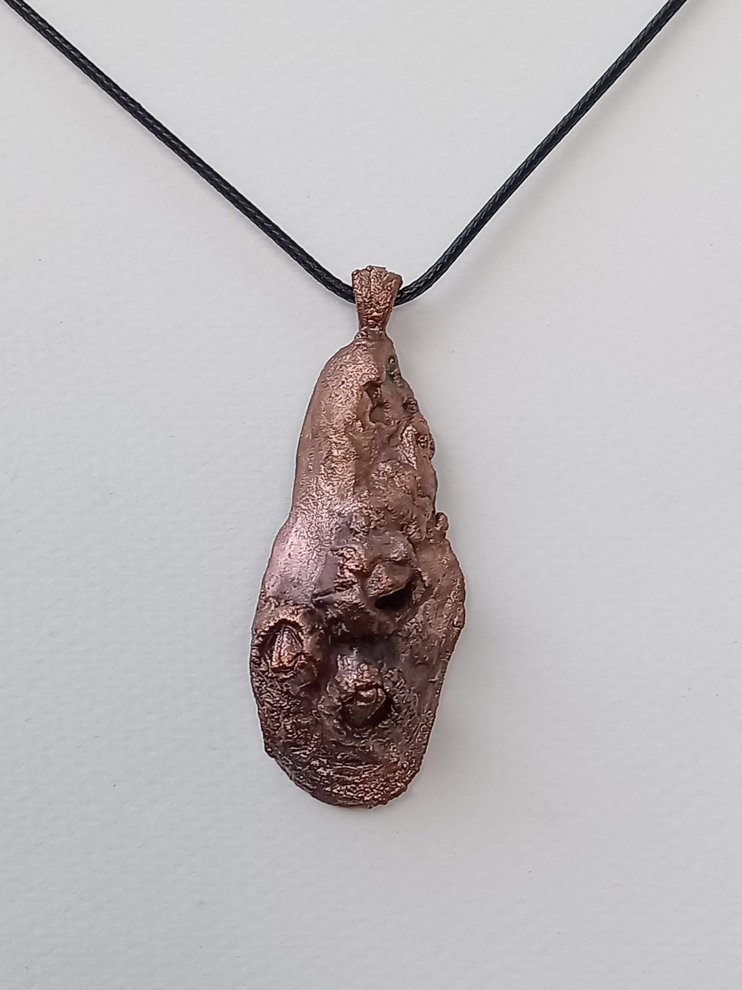 Copper pendant on a black cord against a light gray background