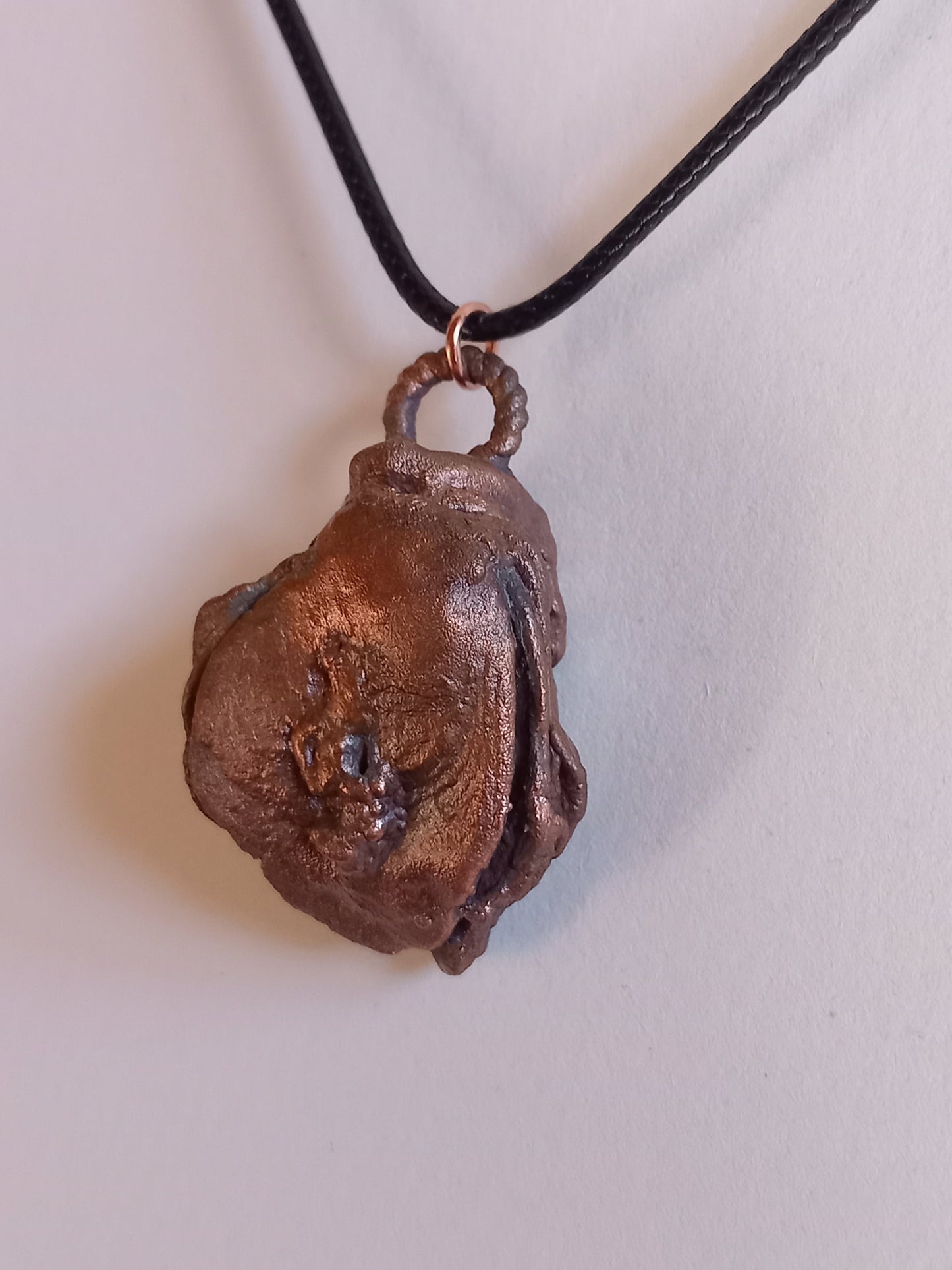 Copper oyster pendant on a black cord against a white background
