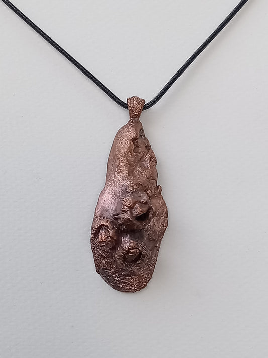 Copper pendant on a black cord against a light gray background