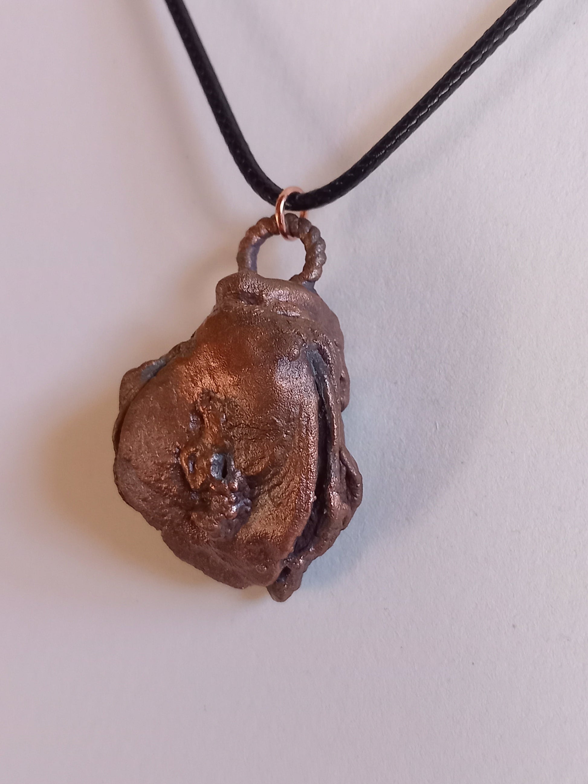 Copper oyster pendant on a black cord against a white background