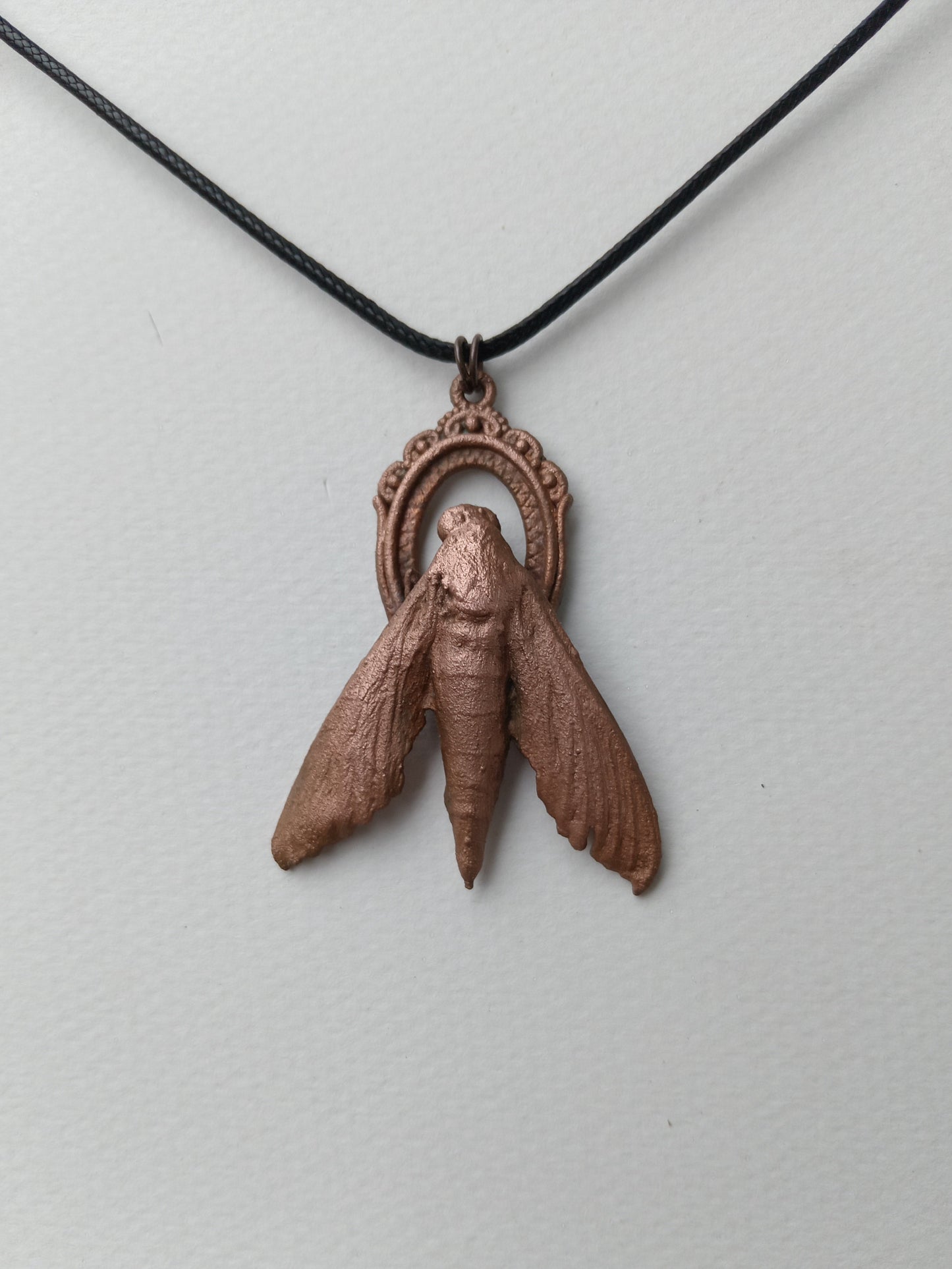 Copper moth pendant on a black cord against a light gray background